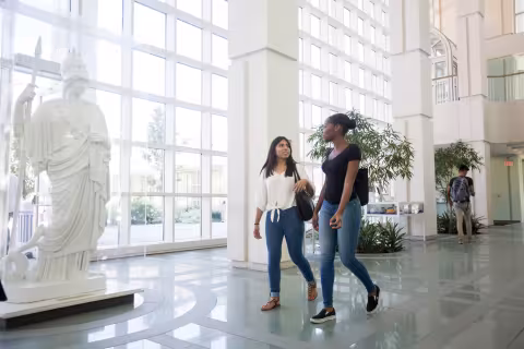 Two students walk past the statue of Minerva, talking to each other.