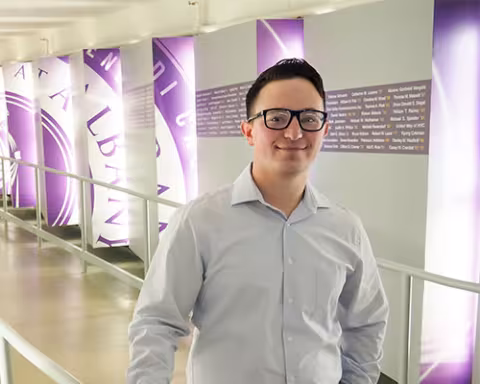 Luc Sandler stands in the entrance to the tunnel for the Massry Center for Business in front of the donor wall.