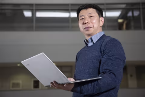 ASRC's Fangqun Yu holds a laptop inside the University Hall atrium.