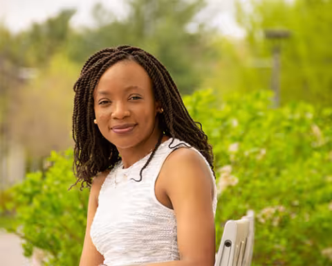 Michelle Wafo poses for a picture in a white dress while sitting on a bench outside.
