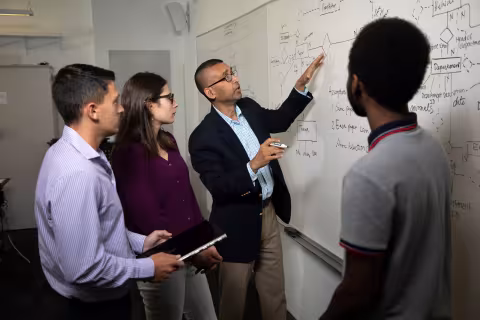 Professor Sanjay Goel works with students inside the Digital Forensics Computer Lab in the Massry Center for Business.