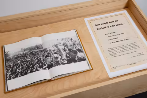A wooden vitrine with a open book and a print out of a poster 