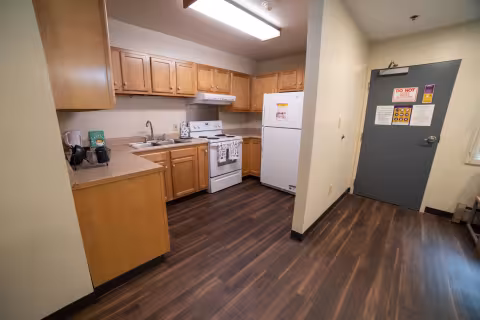 A front door and kitchen, with while appliances and light wood cabinets.