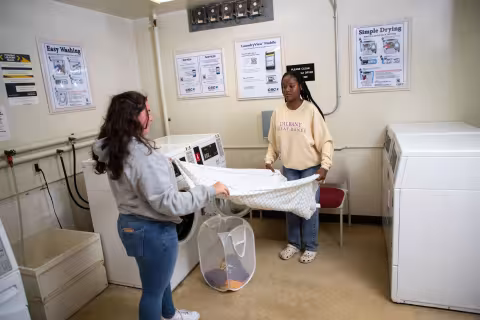 Two students fold a sheet inside the common Laundry Room.
