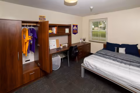 A fully furnished bedroom with a full-sized mattress and bed frame, a chair and desk, and a dresser. 