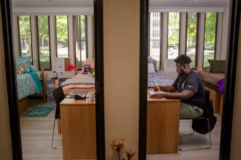 The view into two double rooms through the doorways. A student in a black t-shirt sits at a desk inside one of the bedrooms.