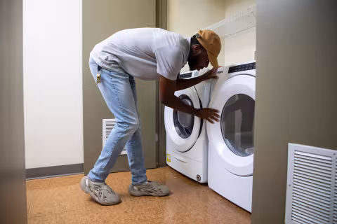 A student leans over to empty a laundry machine inside his Empire Commons apartment.