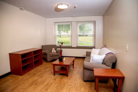 A living room with a soft brown sofa and chair, as well as wood side table, coffee table and book shelf.
