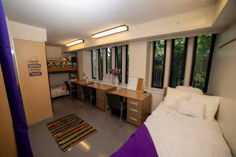 A triple bedroom, with a twin bed, twin bunk beds, three desks and three chairs.