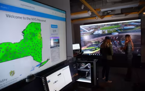 A photo showing screens in UAlbany's xCITE visualization lab, including one displaying a green map of New York and weather data from the New York State Mesonet.  