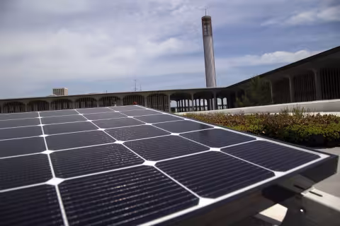 A close-up photo of a solar panel on the roof of the Campus Center with UAlbany's carillon and Academic Podium visible in the background.