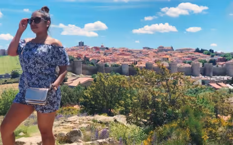 A young woman walks away from 100s of yards of castle walls and behind them a hillside of adobe-topped residences