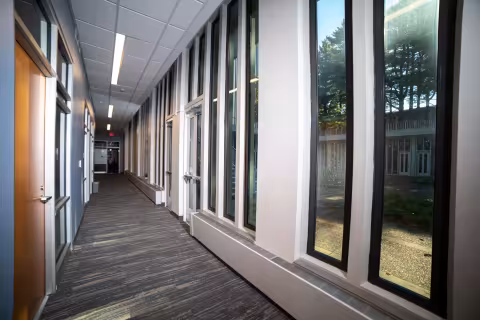 A long hallway, with office doors on one side and floor-to-ceiling windows looking out onto a courtyard on the other side.
