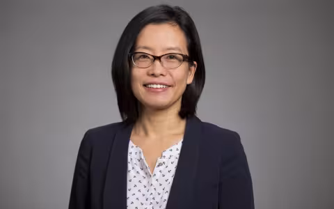 Na Dai, smiling and wearing glasses and a blue blazer