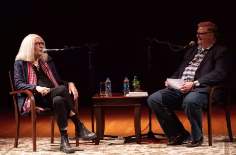 two individuals seated on stage with small table between them