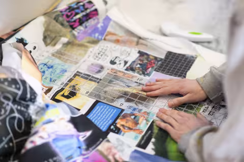 Two hands place a ruler alongside fabric printed with digital collage and meme art. 