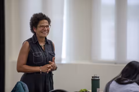 Elizabeth Vásquez, standing at a table in a room in the campus center, welcomes the SPRINTER students. 
