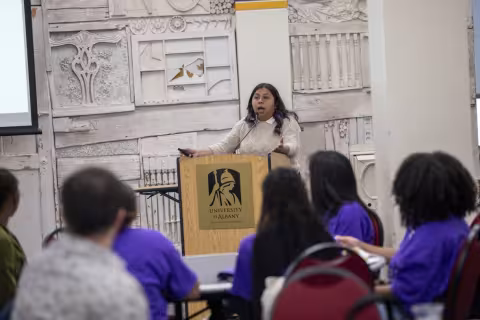 Esperanza Rosas stands at a podium to present her research to the group. 