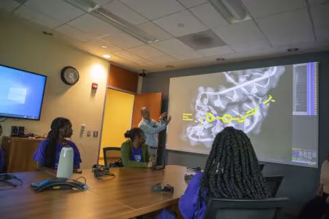 Andy Berglund presents a 3D model of RNA displayed on a pull down screen to the visiting students. 