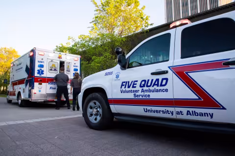 Two Five Quad members close the back doors of a Five Quad ambulance, which is parked in front of a Five Quad SUV.