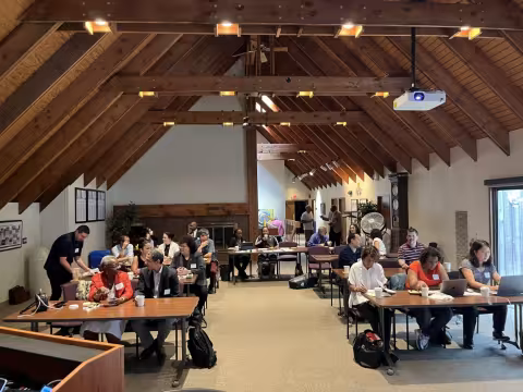 A group of over twenty faculty members sit at tables arranged in front-facing rows on the second story of UAlbany’s Alumni House, waiting for the meeting to begin. 