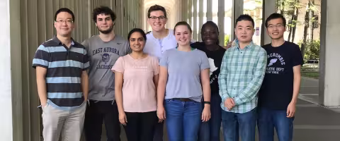 Eight members of The Wang Group stand together on a campus sidewalk at the University at Albany.