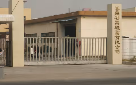 A one-story tan brink building, adorned with a blue awning and surrounded by pillars and metal fencing. Chinese lettering on one pillar translates to "Panyu Li Chang Shoes Co., Ltd."