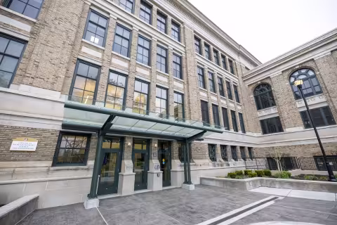 An exterior shot of a tan brick building and gray stone entry plaza.