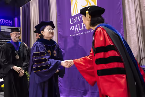 A UAlbany PhD graduate shakes hands with Provost Carol Kim as she crosses the stage.