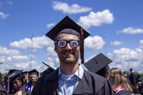 A UAlbany graduate wears black and white glasses that say 2024 across them.