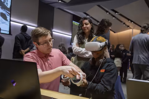 A middle school student tries on a virtual reality headset as a man helps during Showcase Day 2024.