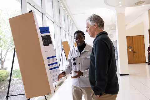 A student explains his research to an older visitor during Showcase Day 2024 inside the Lecture Center concourse at UAlbany.