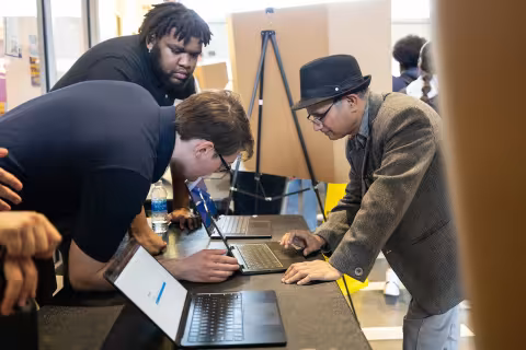Two students display their research on laptops with UAlbany Professor of Computer Science Pradeep Atrey.