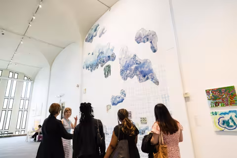 A woman discusses her large piece of artwork that his displayed on a two-story wall to four visitors inside the UAlbany Art Museum.