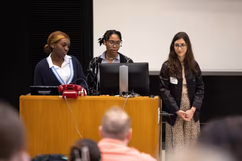 Three students present their research inside the Lecture Center at UAlbany during Showcase Day 2024.