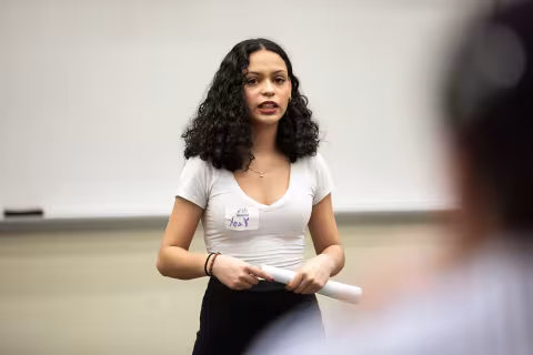 A student dressed in a white blouse and black leggings with dark hair presents her research inside the lecture center at UAlbany on Showcase Day 2024.