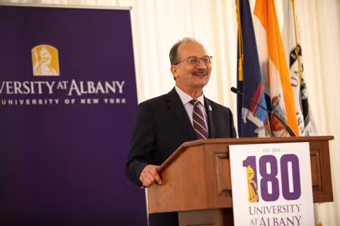 UAlbany President Havidan Rodriguez oversees the closing ceremonies of Showcase Day 2024 at UAlbany standing at a podium with a sign that says 180 University at Albany.
