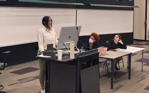 A student stands at a podium while presenting on a panel at UAlbany Showcase