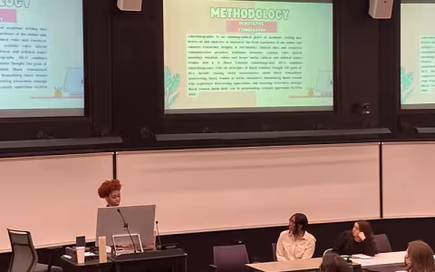 A student stands at a podium and explains their methodology while presenting on a panel at UAlbany Showcase