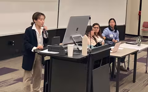 A student stands at a podium and holds a microphone while presenting at UAlbany Showcase