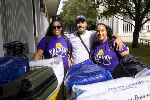 A new student wearing a purple UAlbany shirt stands with her family on move-in day.