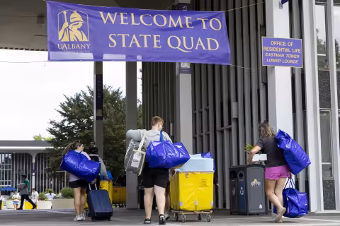 A family wheels dorm items past a "Welcome to State Quad" sign.
