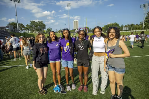 Six young women smile for a group photo on the football field during Great DANEtopia. 