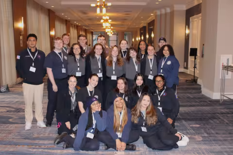 22 Five Quad student volunteers pose for a photo wearing their uniforms and conference lanyards at an awards banquet.