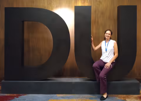 Jessica Mathis stands in front a large Deloitte logo.