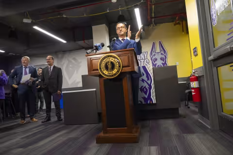 UAlbany Vice President for Student Affairs and Enrollment Michael Christakis claps at the podium during the esports arena unveiling.