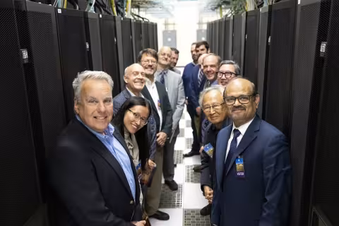 Two rows of smiling people lean toward each other between two large computer server racks.