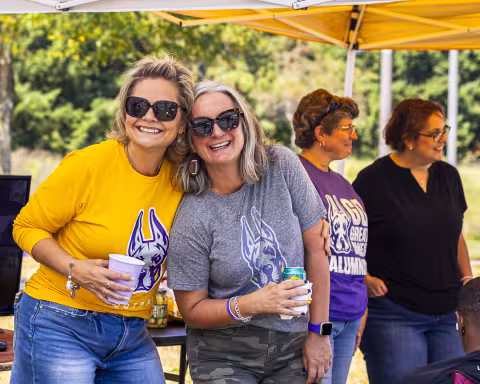 Two women wearing shirts with the Great Dane logo pose and smile for a photo under a pop-up tent.