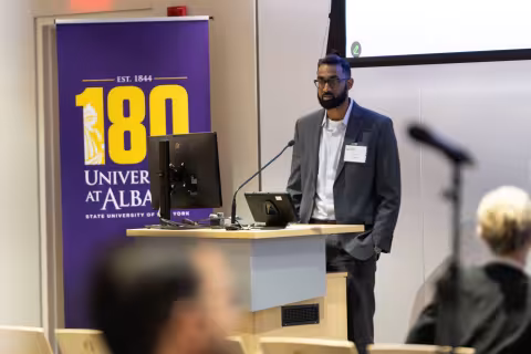 A presenter stands at the podium during R&E Week at UAlbany in October, 2024.