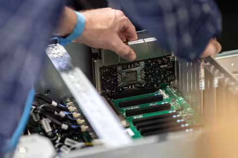 A close-up image of human hands inserting a silver and black computer card into a machine.